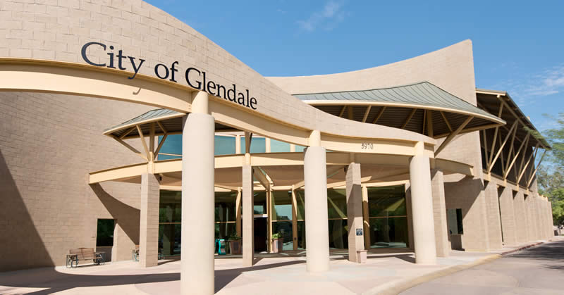 Entrance of the City of Glendale building with curved architecture, large pillars, and glass doors under a clear blue sky.